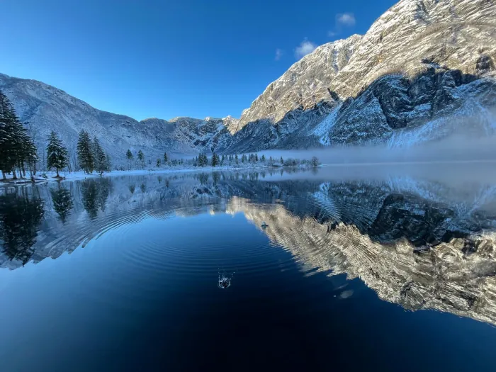 Bohinjsko jezero v jutranji megli, gore se zrcalijo v mirni vodi